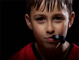 A little boy holding a mouthguard between his teeth to prevent dental emergencies in Herndon