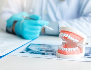 Dentist’s gloved hands at desk with papers, X-rays, and model teeth