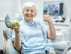 An older man smiling while a dental hygienist shows him how to clean his dentures