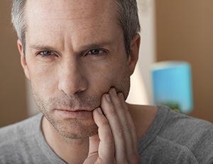 A middle-aged man holding his cheek as a result of a severe toothache