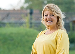 A middle-aged woman wearing a yellow blouse and smiling after receiving dental implants