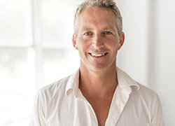 A middle-aged man wearing a white button-down shirt and smiling after learning he is eligible for dental implants