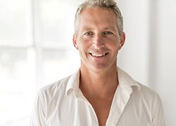 A middle-aged man wearing a white button-down shirt and smiling after learning he is eligible for dental implants