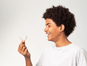 Teenage boy smiling while holding clear aligner