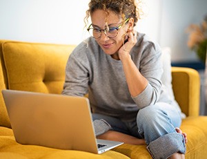 Woman with glasses smiling while looking at laptop