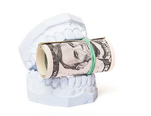 model of teeth holding rolled up money