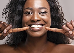 A woman smiling and pointing to her teeth that are damage-free in Herndon