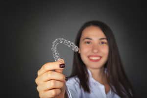 woman smiling holding an invisalign aligner