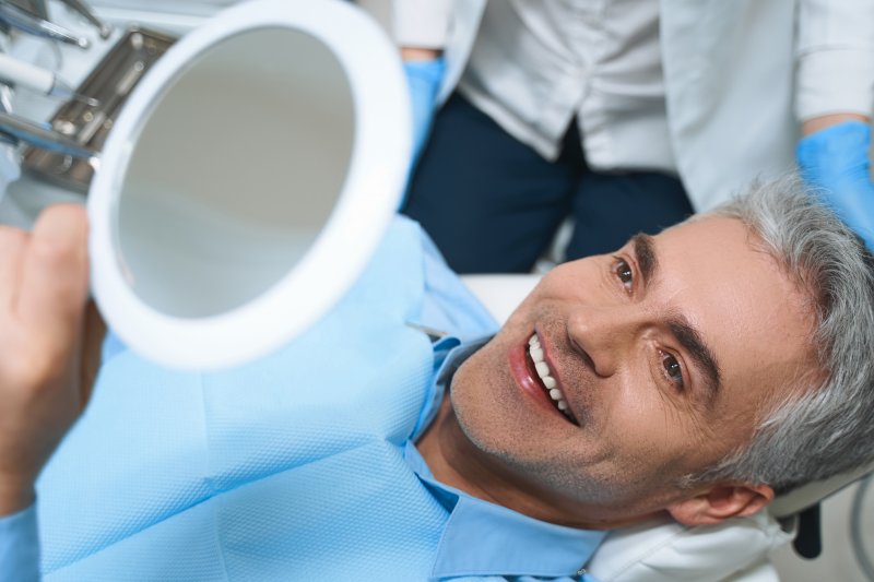 an older man lying back in the dentist’s chair looking at his new smile in the mirror