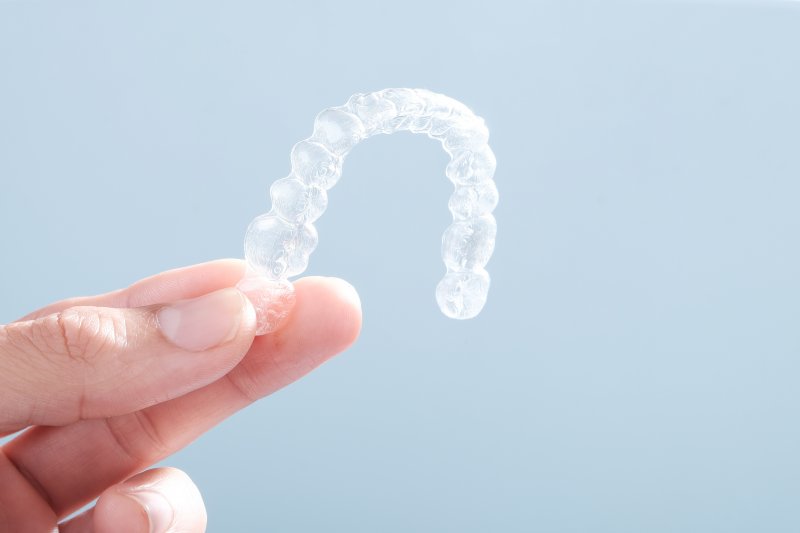 an up-close image of a person holding a clear Invisalign aligner
