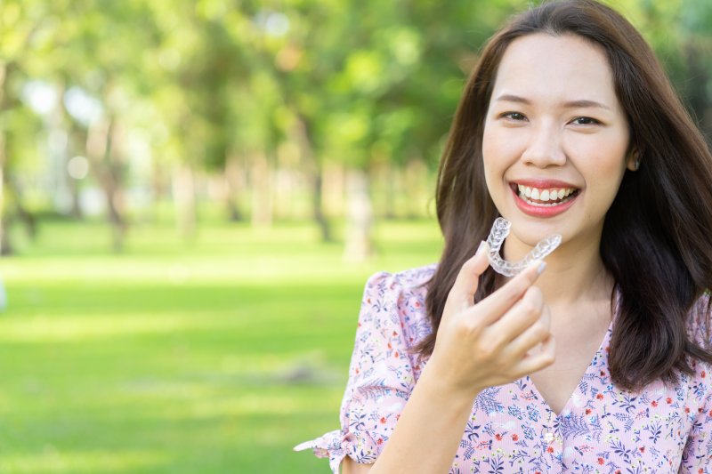 Woman in floral shirt smiling while holding Invisalign clear aligner