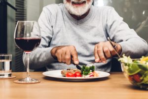 Nose down view of a man eating dinner at a table with a glass of red wine